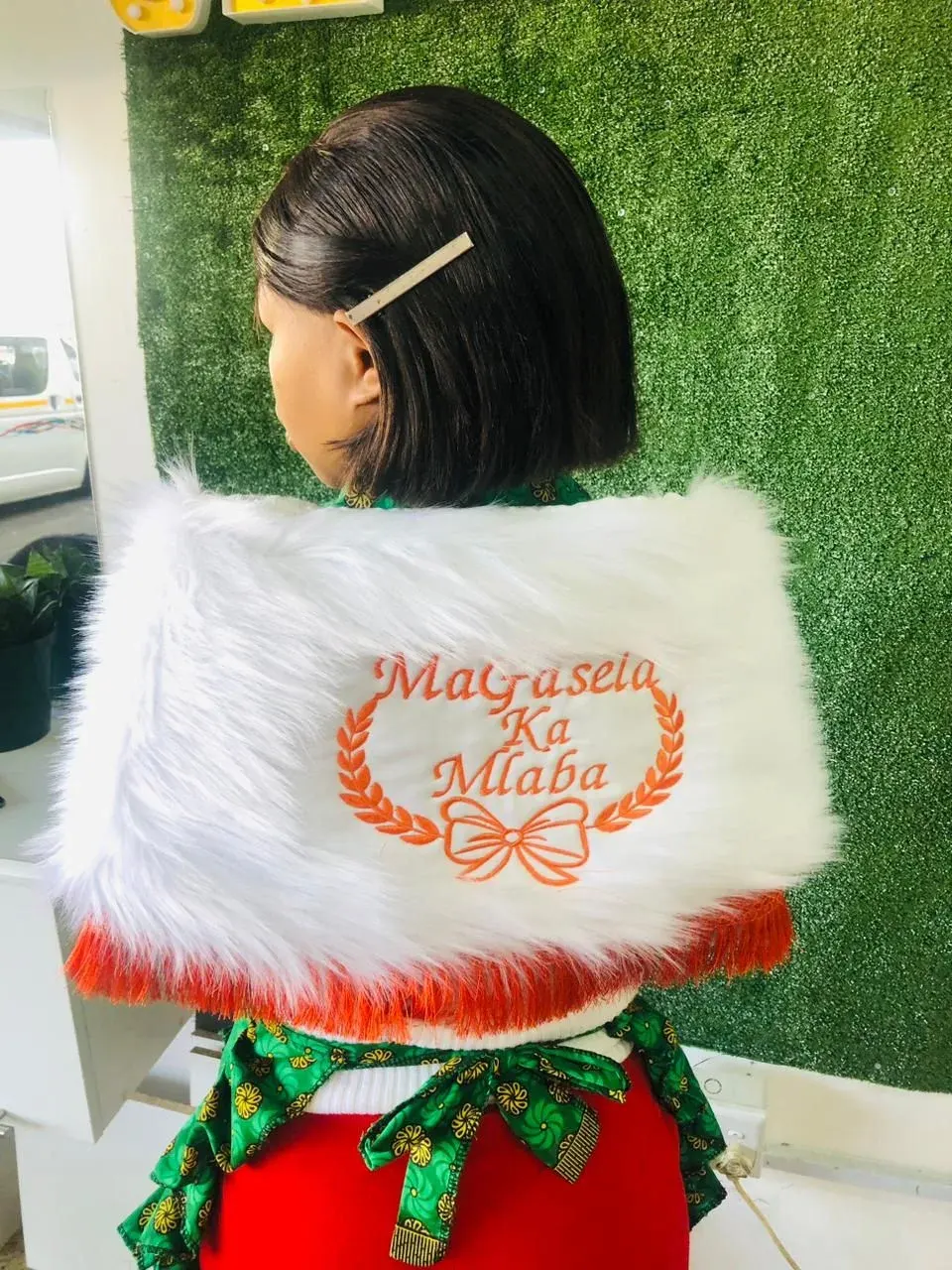 White faux-fur shoulder wrap embroidered with a clan name in orange thread